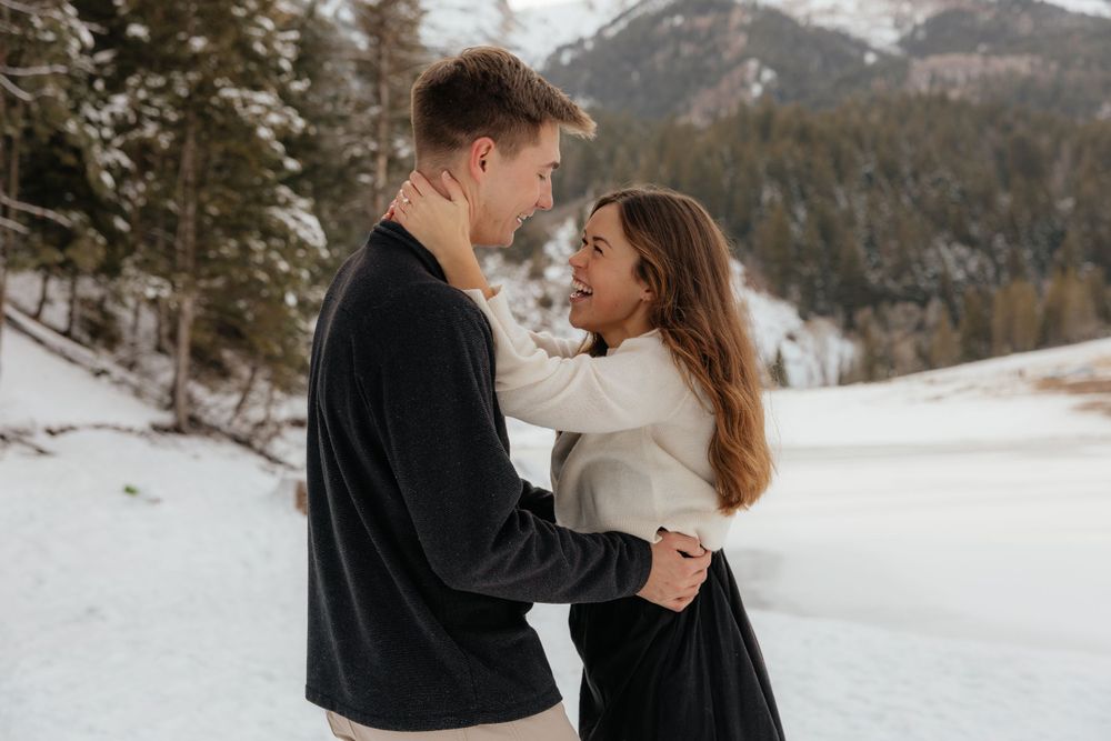Couple embracing and gazing into each other eyes in a snowy winter mountain landscape.