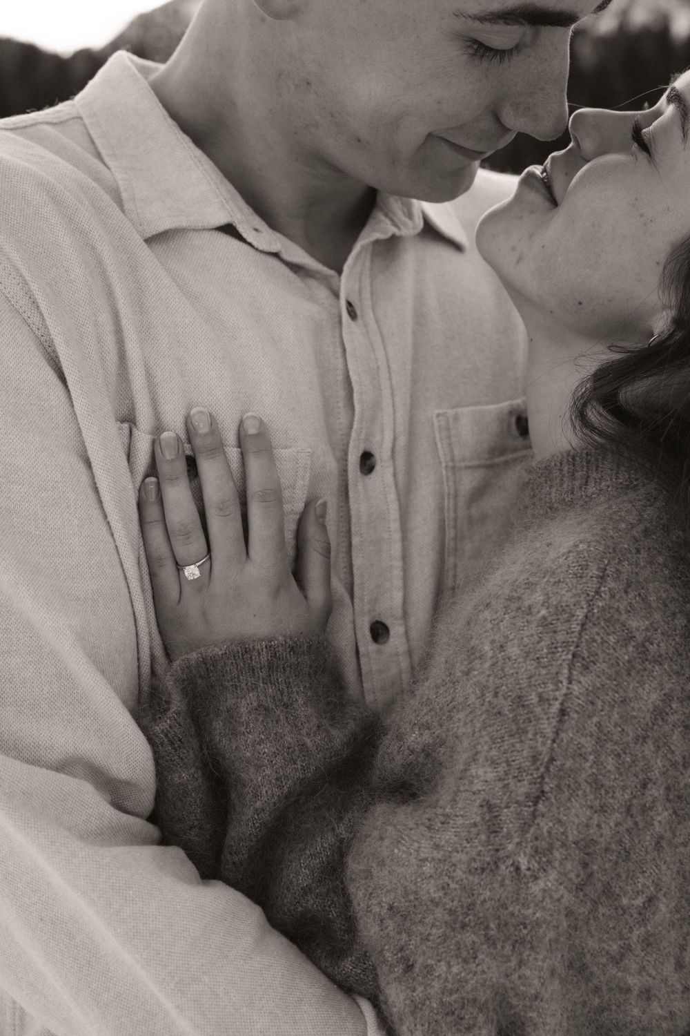 Black and white close-up of couple about to kiss, engagement ring visible on womans hand.