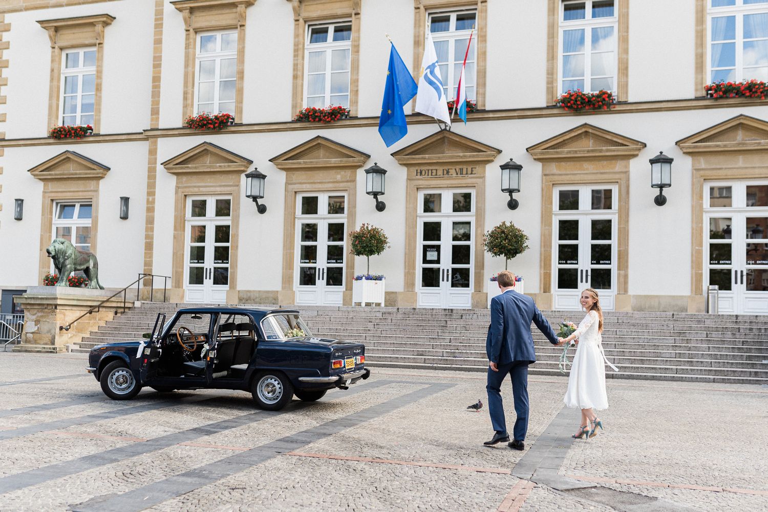 Vintage black car parked in front of an elegant European building with classic architecture and stone stairs.