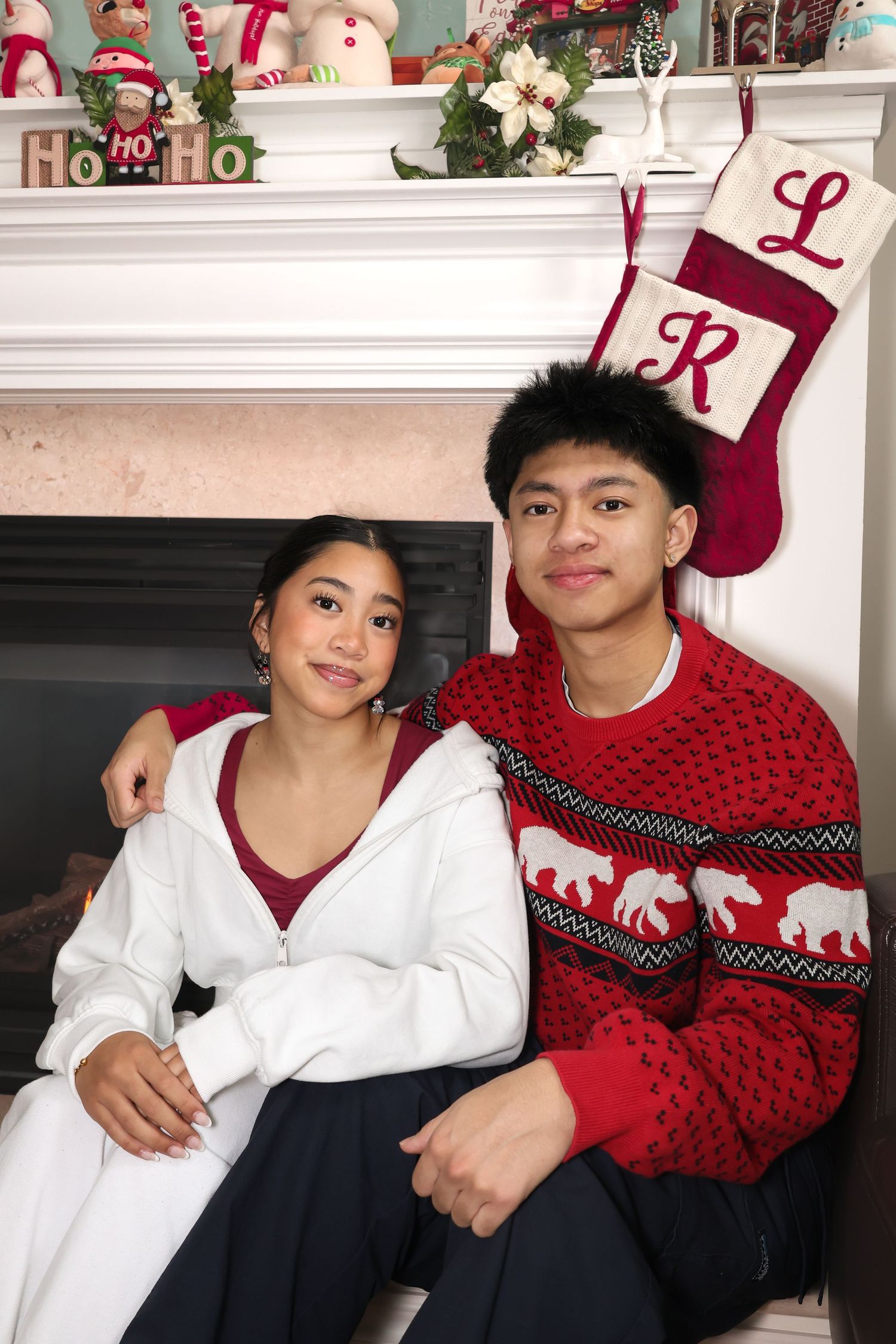 Siblings in red and white posing for a Christmas photo in front of a fireplace