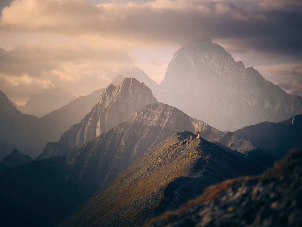 Dramatic panoramic view of wedding in misty mountain peaks at sunrise with golden sunlight filtering through clouds.