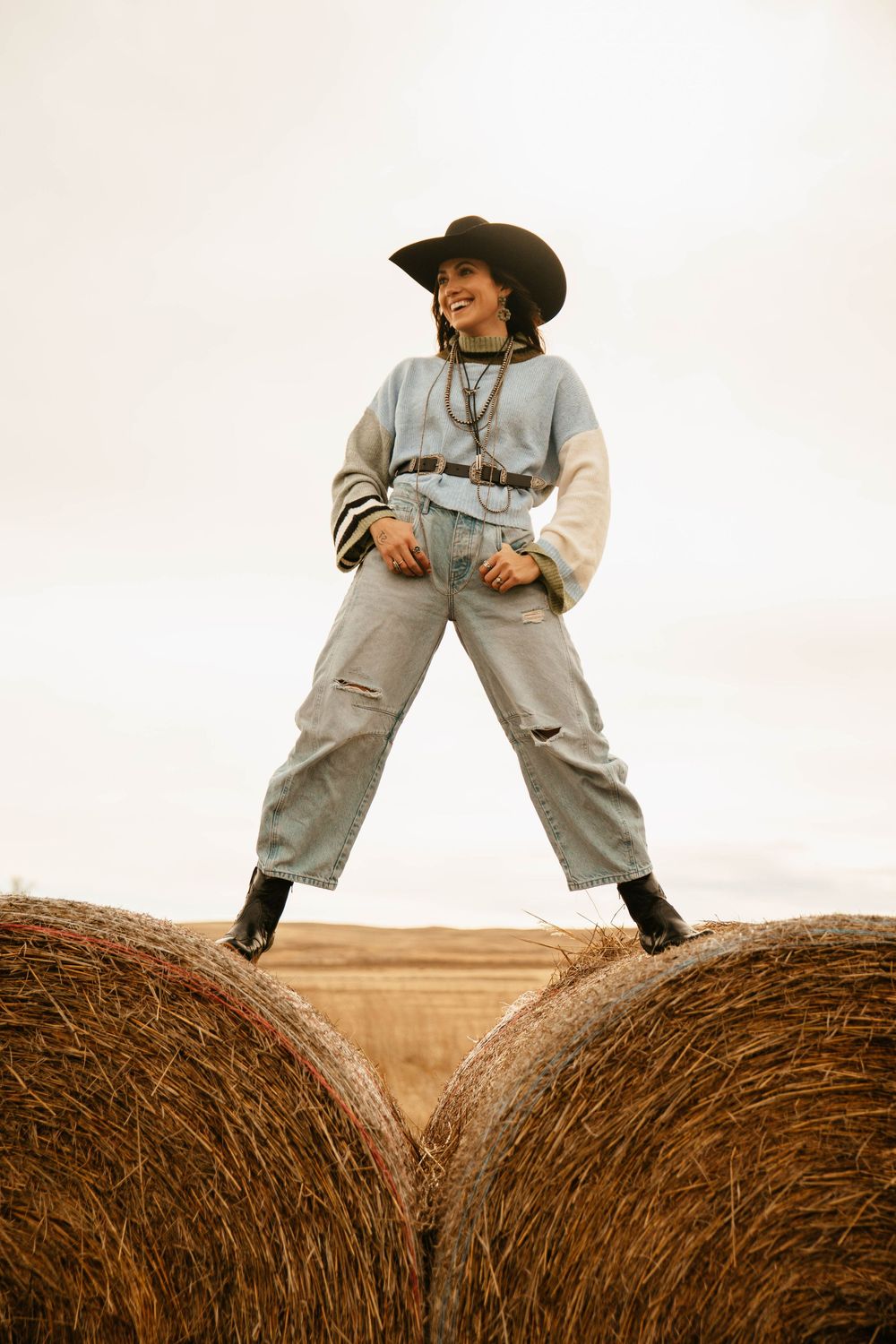 A sequence of images showing someone in overalls climbing and posing on top of large round hay bales in a field.