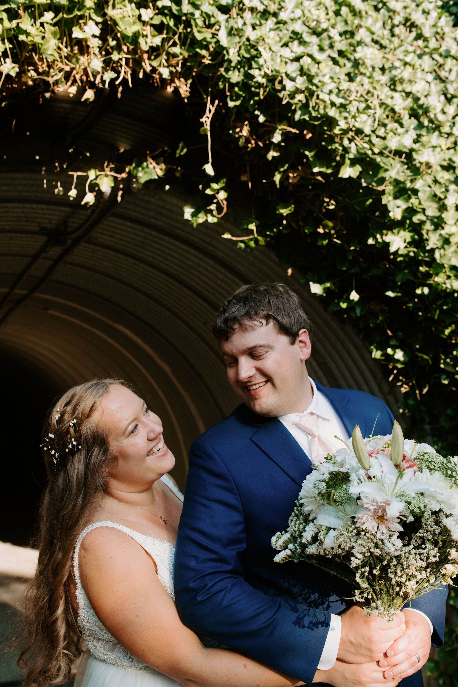 Wedding couple sharing joyful moment under ivy-covered archway.