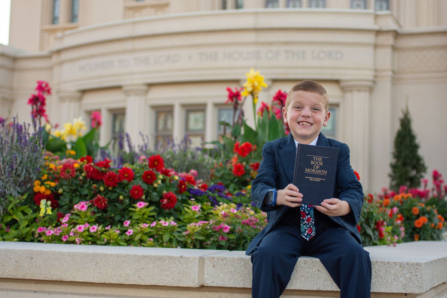 boy poses with the Book of Mormon in front of the Springville temple for his baptism pictures.