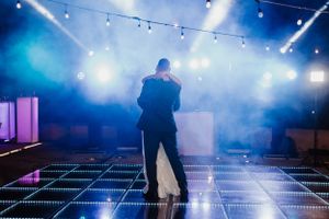 A silhouetted performer stands on an illuminated dance floor with blue atmospheric lighting and fog effects during a show.