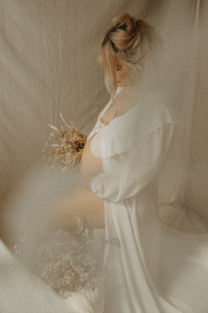 pregnant woman holds dried flowers in dreamy vintage-style portrait with soft beige tones.bromley and Beckenham maternity photography