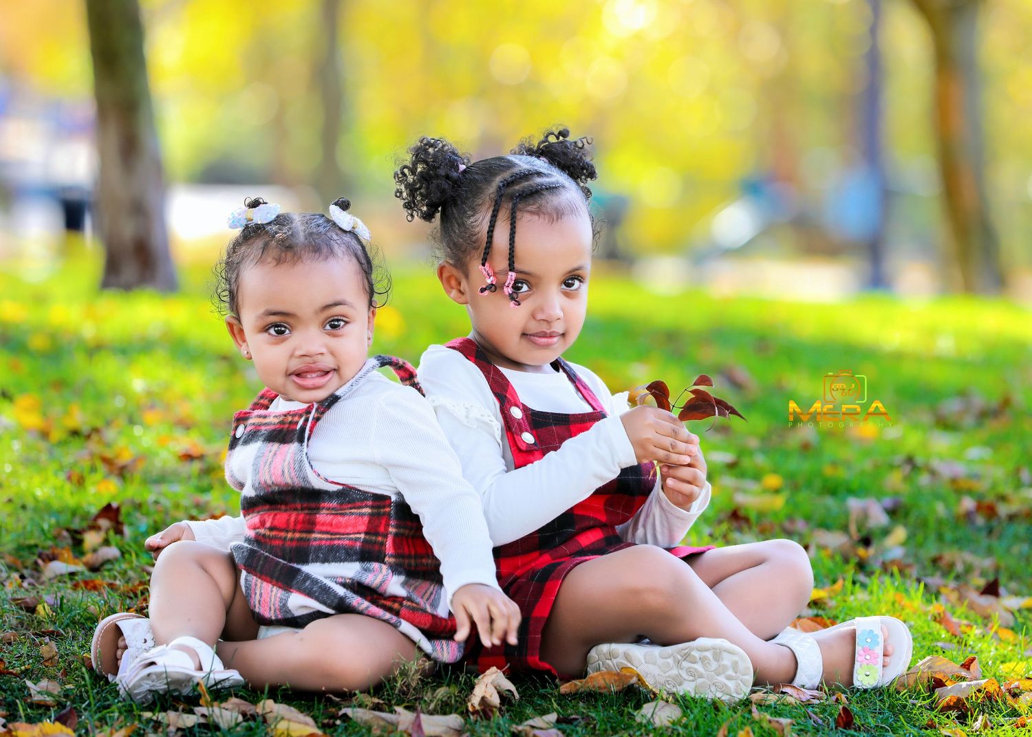 Two small children sit together on autumn leaves wearing matching red and white outfits.