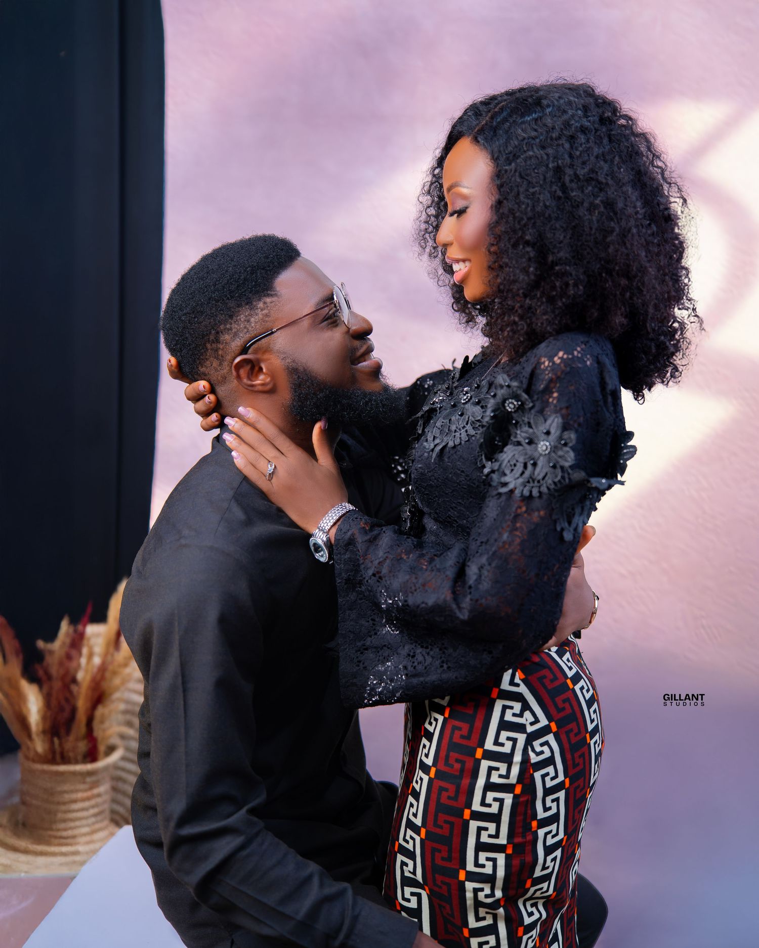 Romantic couple pose intimately against pink backdrop during engagement photoshoot.