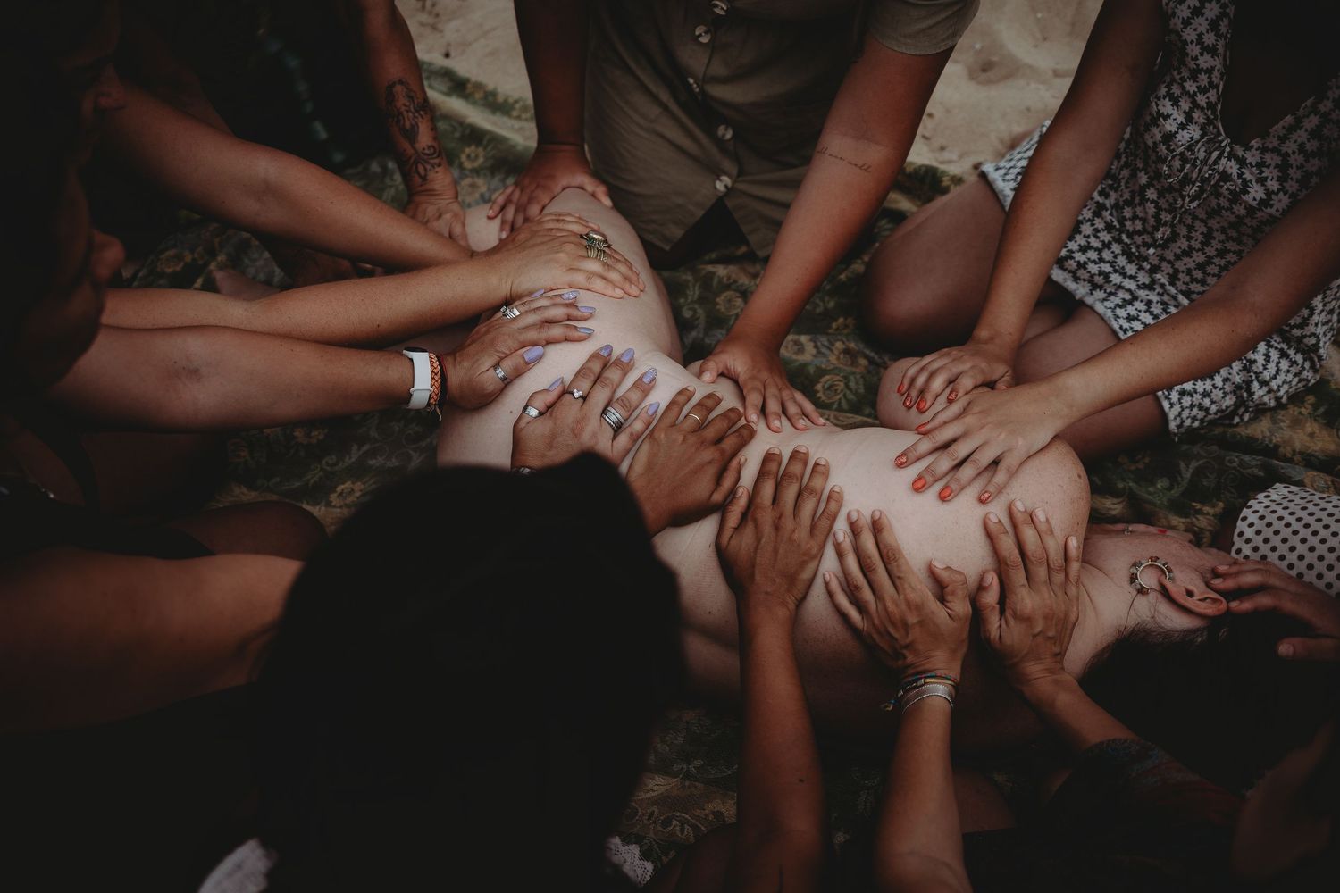 foto colorida mulher deitada em ritual de cura com varias mãos sobre ela em circulo feminino em  Portugal