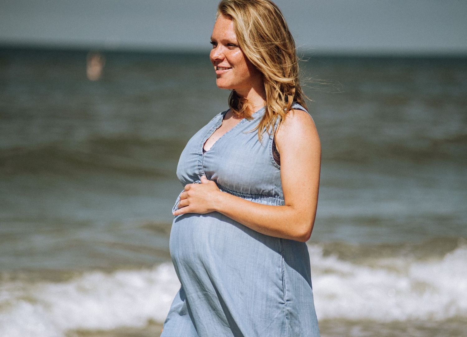 A serene outdoor maternity photo on a beach, with soft waves and a glowing sunset.