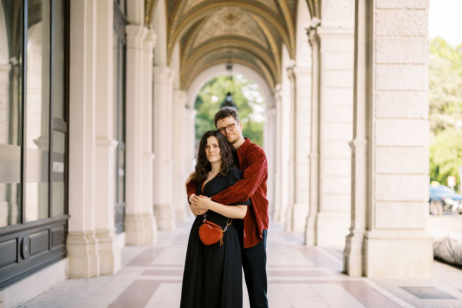 A couple embraces while standing in an elegant arched colonnade with classic architectural details.