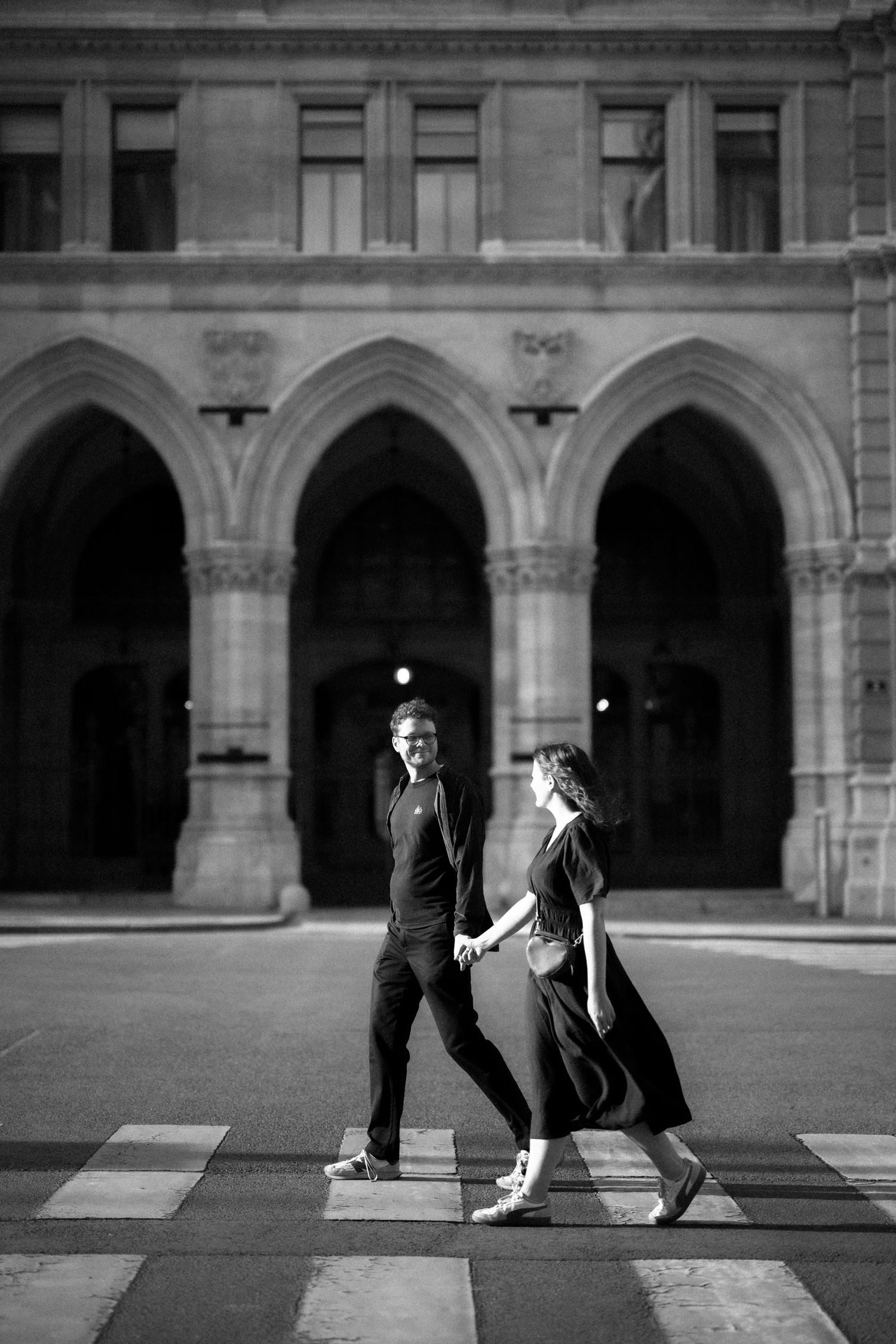 A black and white photograph showing a romantic moment at a grand building with arched gothic architecture.