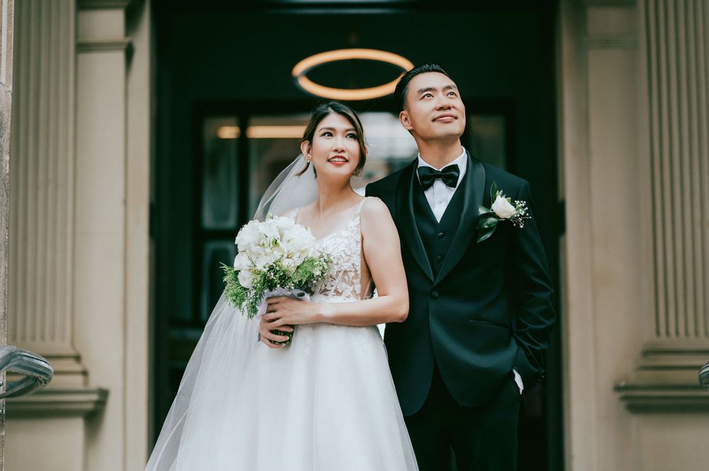 Wedding couple poses together with white bouquet in front of classic columns of a building.