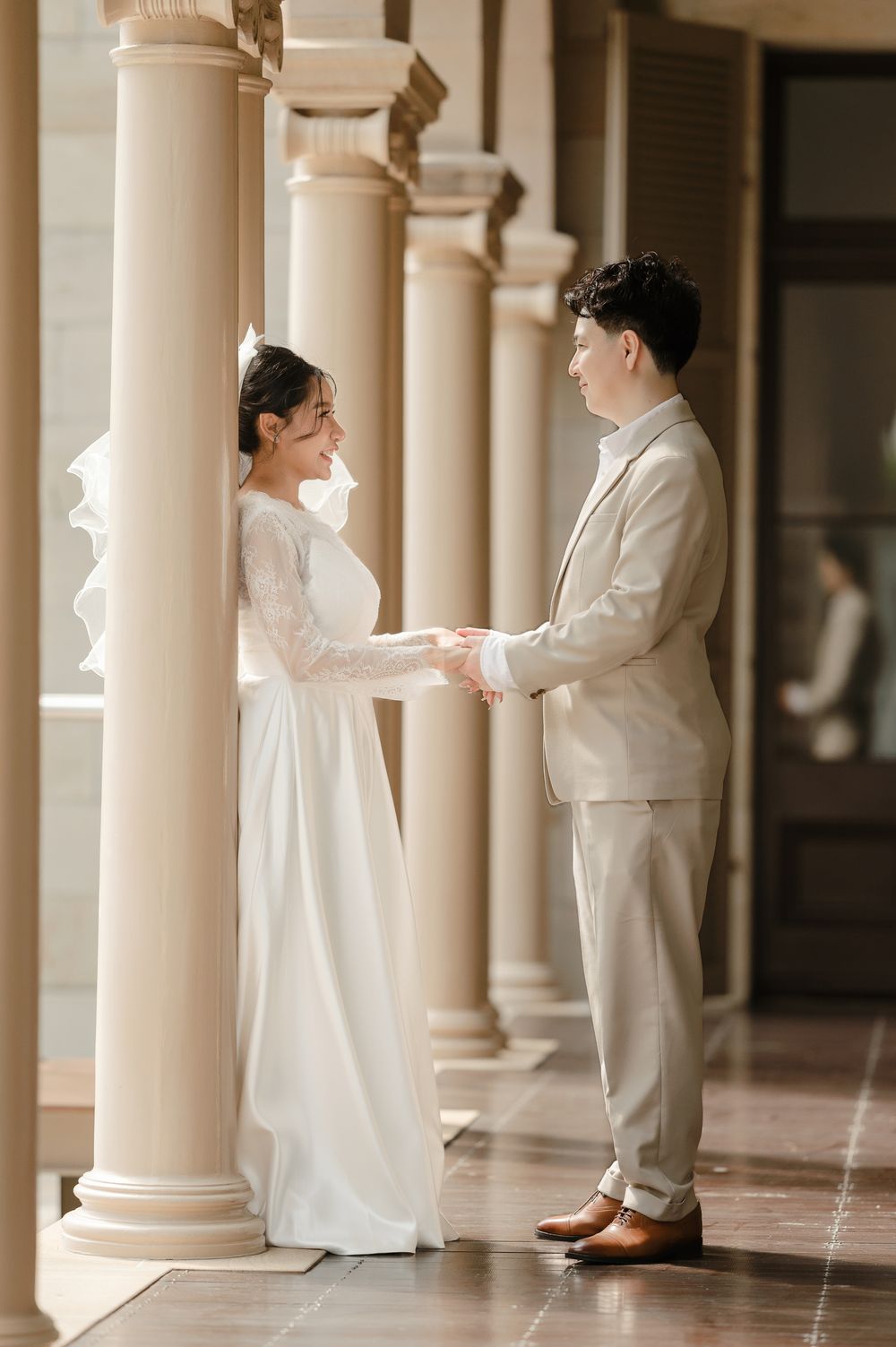 Couple holds hands in elegant wedding attire between classic white columns.