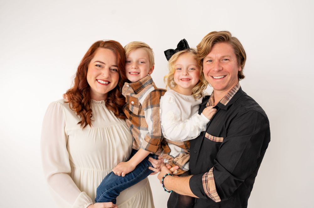 Family poses in white and cream colored outfits against bright studio backdrop.