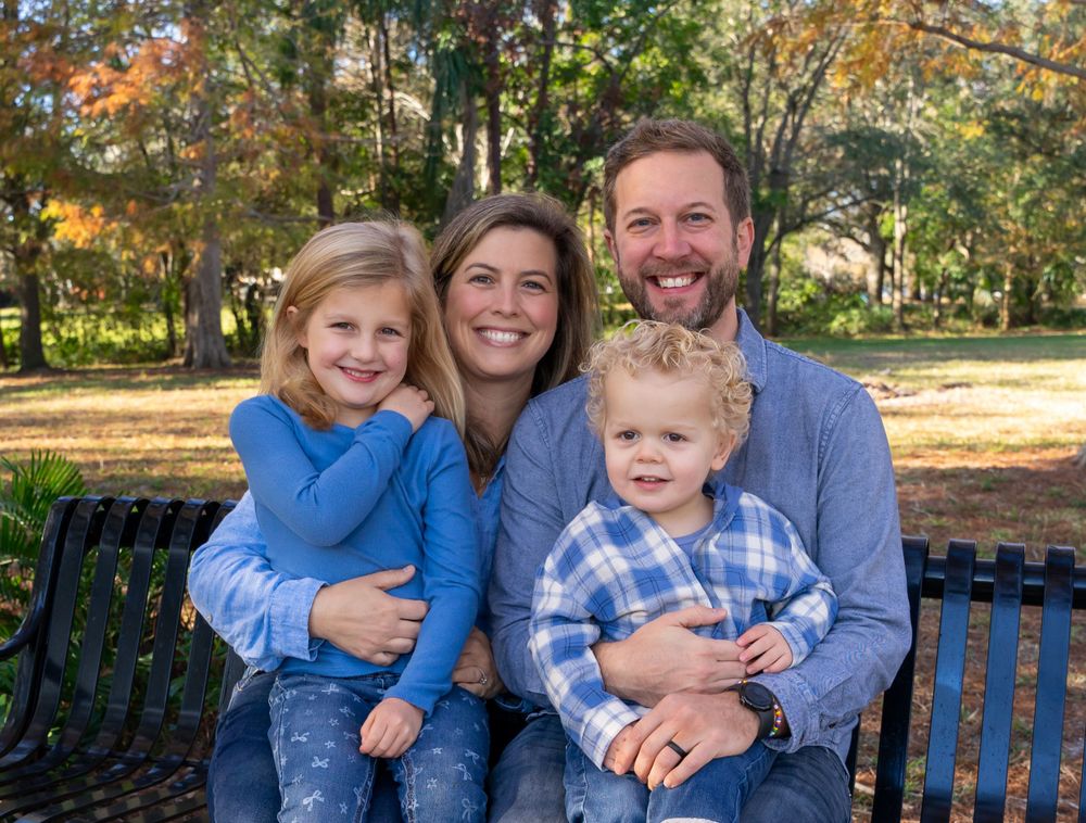Family sitting together on a park bench surrounded by autumn trees and golden light.