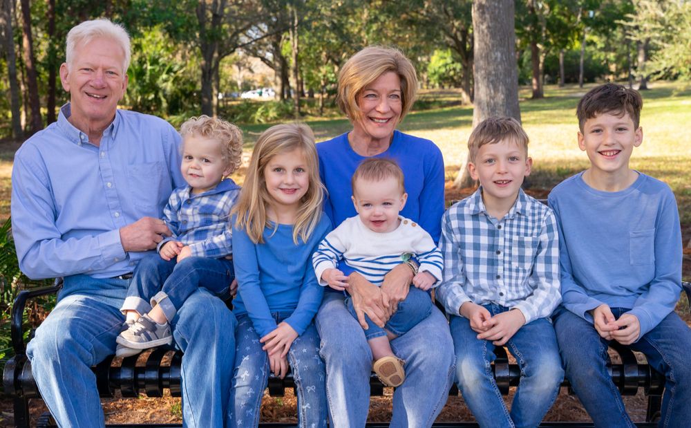 Multi-generational family portrait taken outdoors on a wooden bench during autumn.