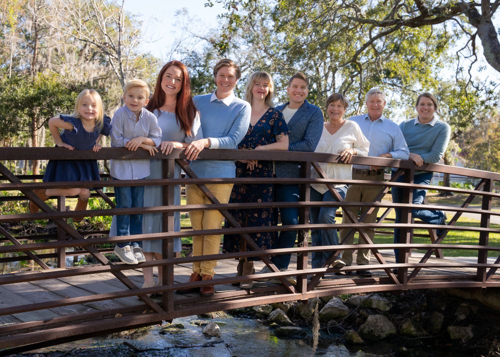 Extended family gathers on wooden bridge in outdoor park setting.