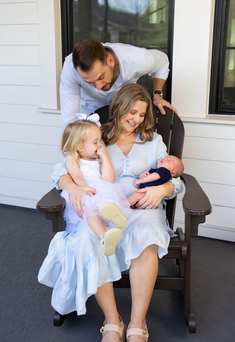Family shares tender moments on porch bench in soft lighting.