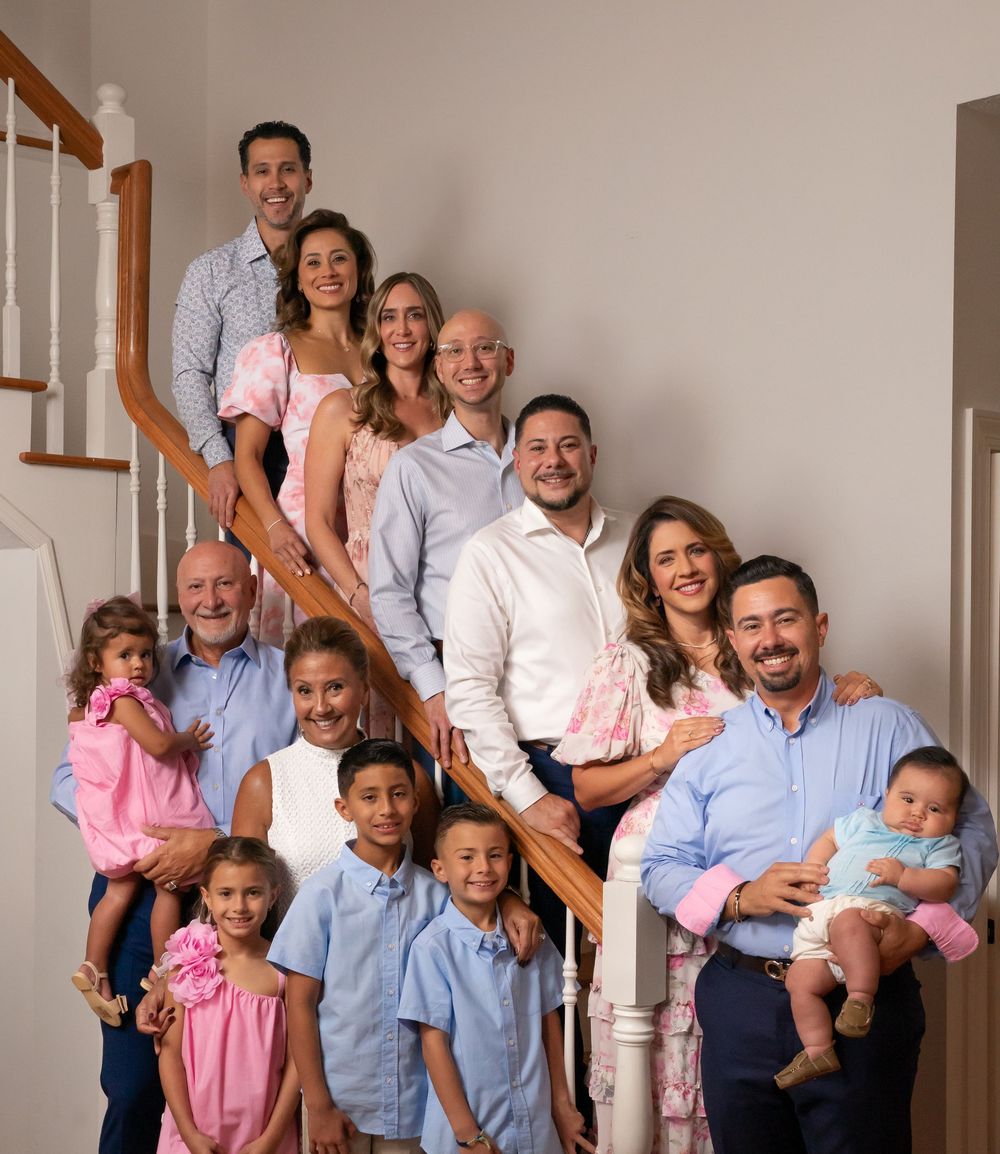 Large multi-generational family posing together on a staircase, smiling, dressed in coordinated pink and blue outfits.