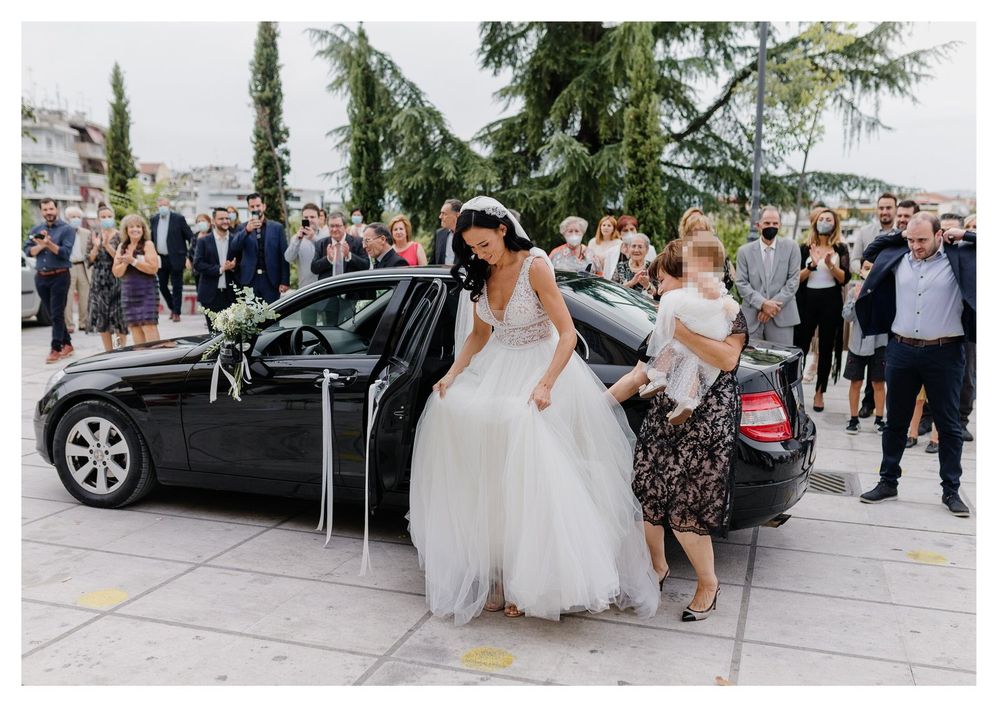 Bride exiting decorated wedding car with assistance from wedding party.
