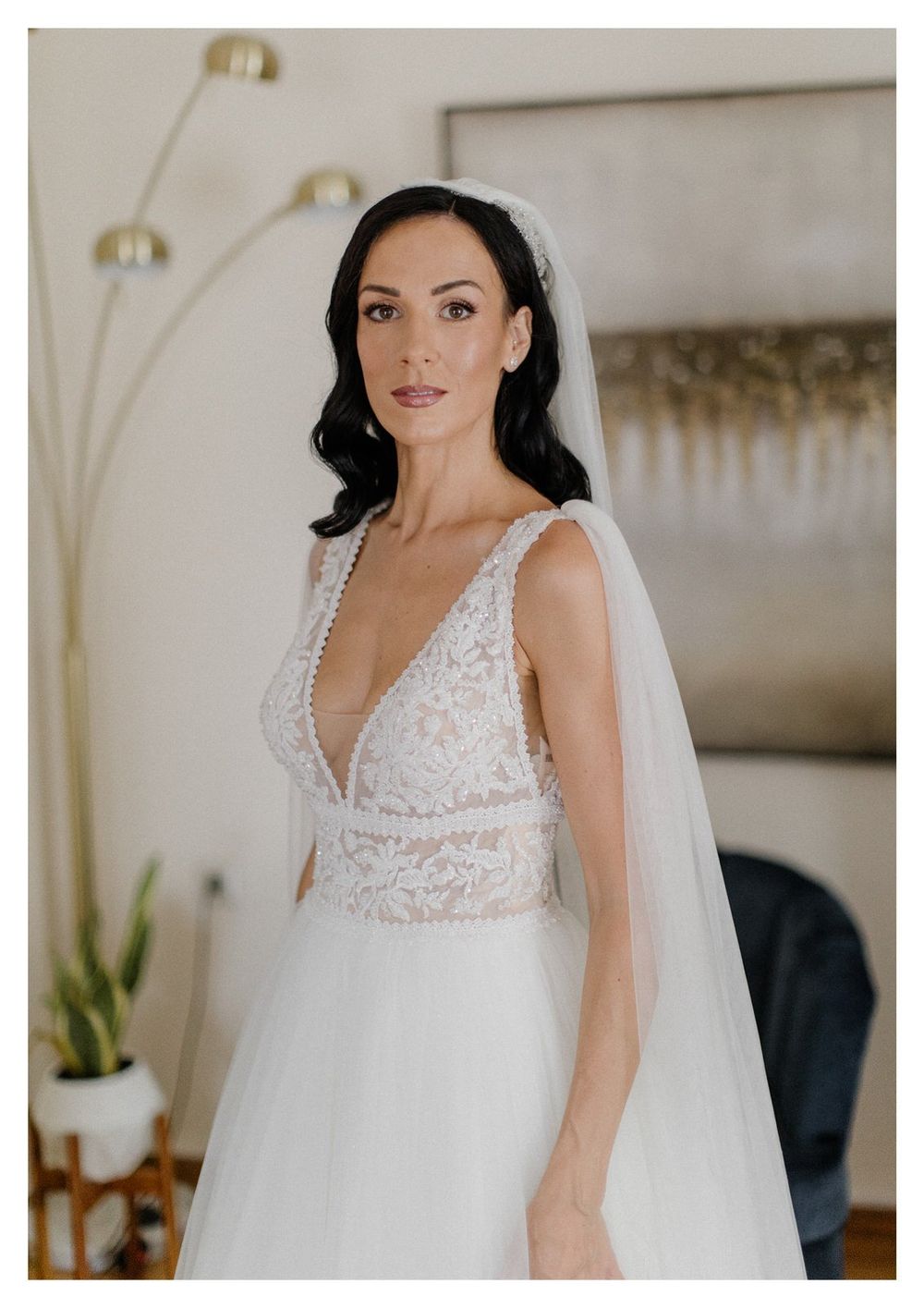 Elegant bride wearing a deep V-neck lace wedding gown with tulle skirt and flowing veil.