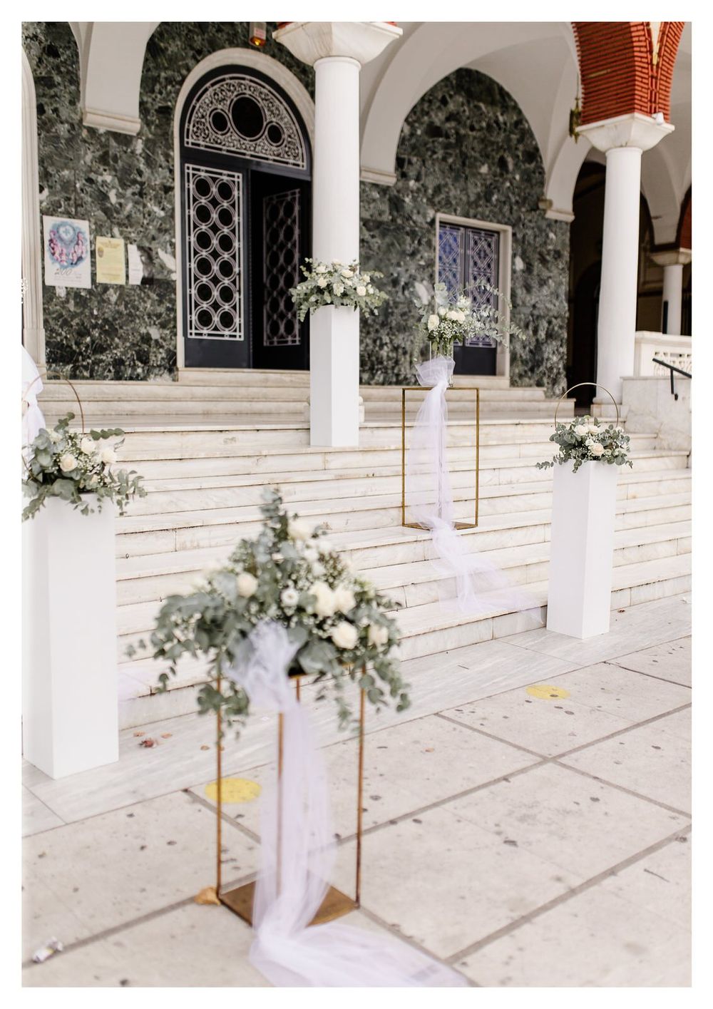 White floral arrangements on gold stands decorating church entrance steps.