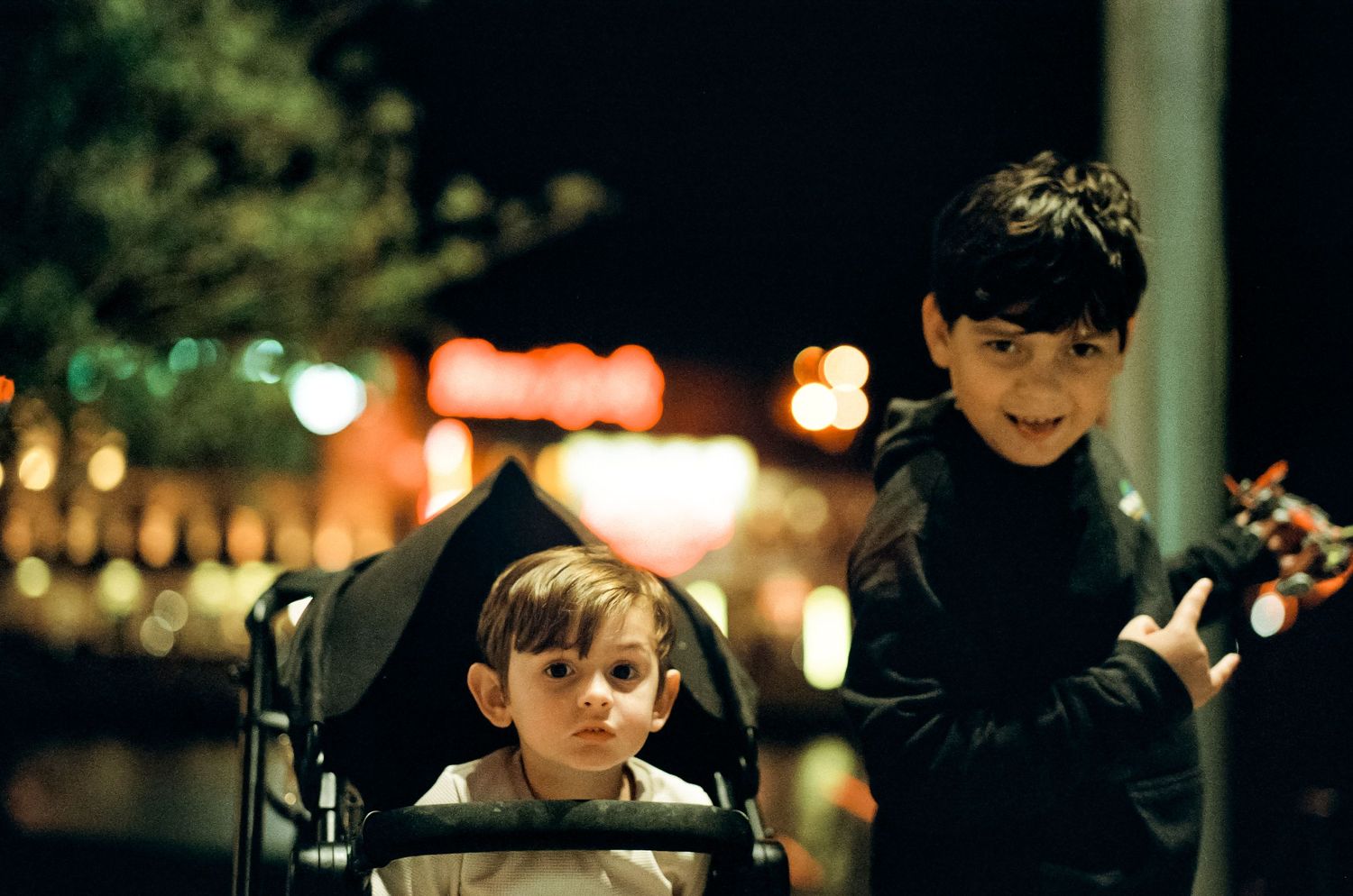 Two children sit together at night with festive holiday lights glowing in the background at Disney World.