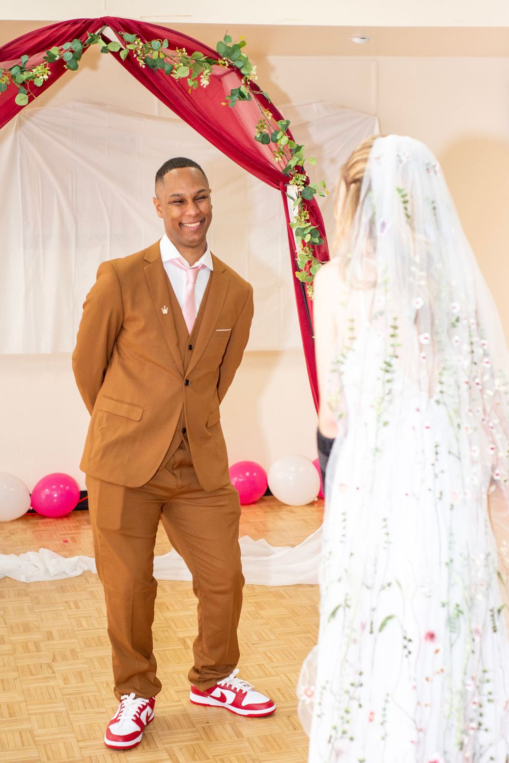 Wedding ceremony setup with red drapery and floral arch decorations in an indoor venue.