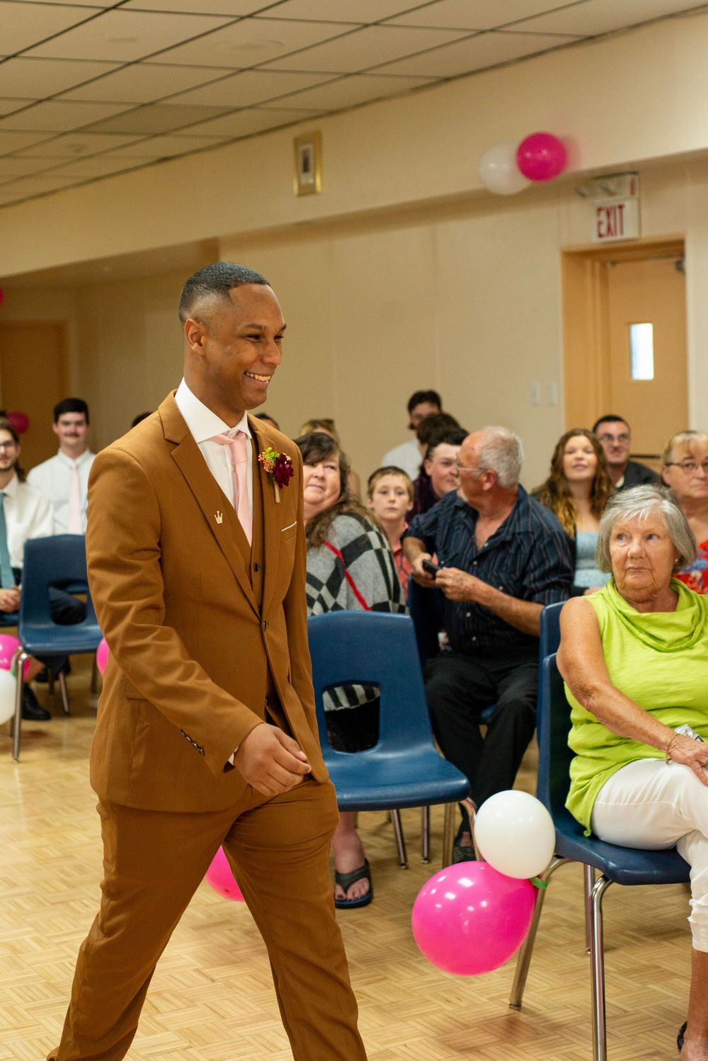 Wedding guest in stylish brown suit walking through event venue decorated with pink and white balloons.