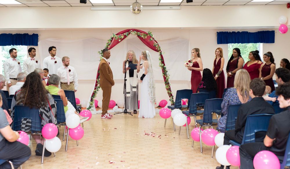 A wedding ceremony in progress under an arch with pink balloons and guests watching.