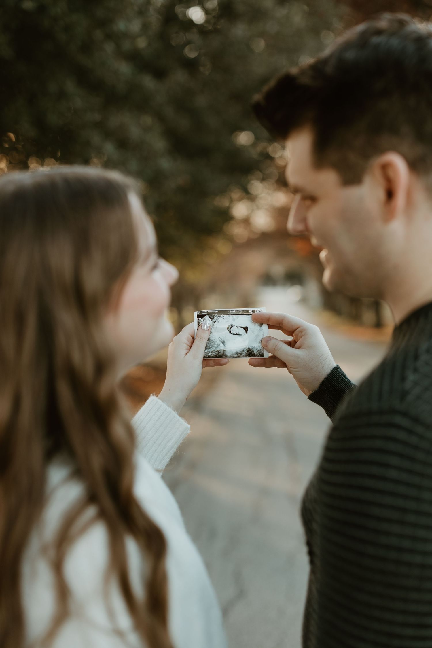 Couple looking at ultrasound photos together during sunset in a park.
