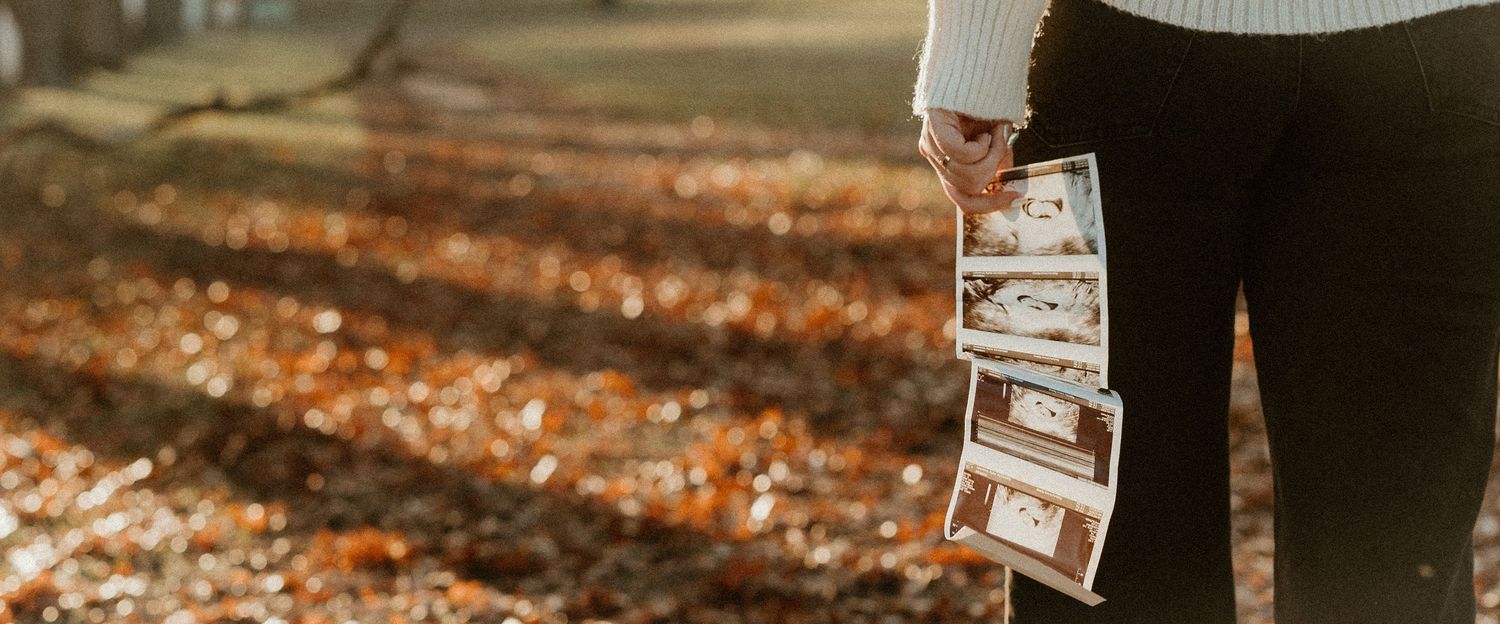 Person holding ultrasound photos against autumn leaves on the ground.