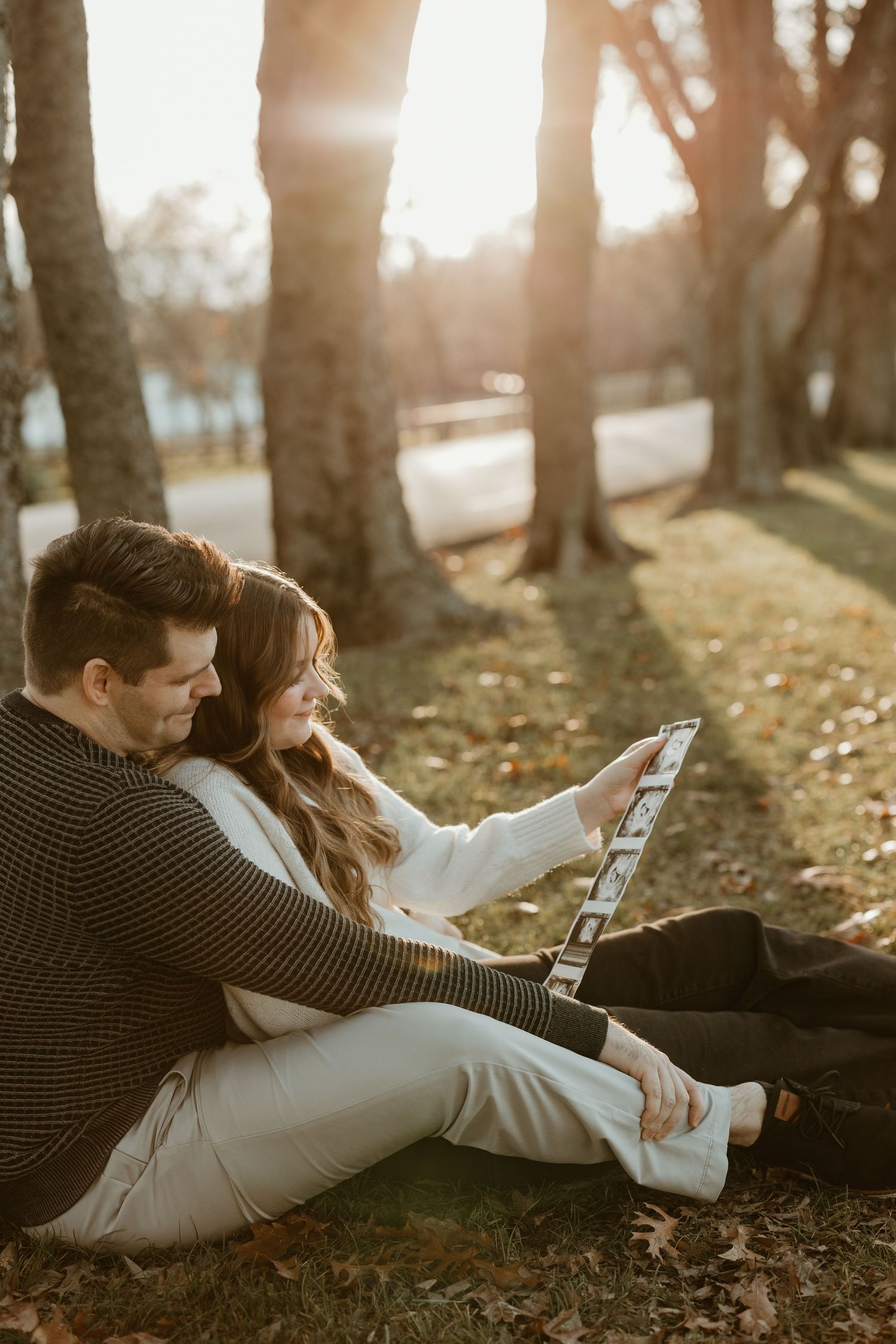 Couple sitting on autumn ground looking at ultrasound photos together.