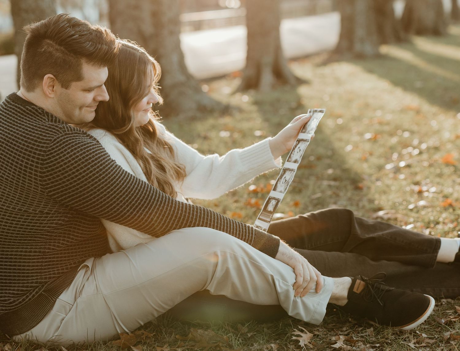 Couple sitting on grass viewing ultrasound photos during autumn photoshoot.