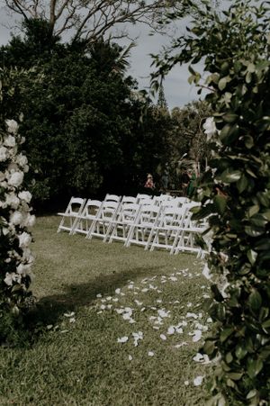 Garden wedding venue with white chairs and flower petals lining the aisle.