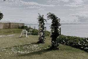 Oceanside wedding arch decorated with greenery against coastal backdrop.
