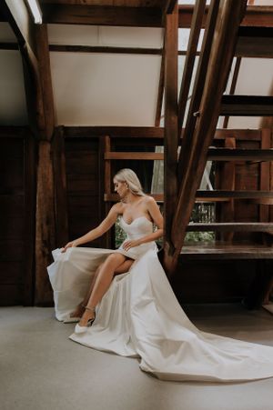 A bride in a flowing white dress poses elegantly in a rustic wooden interior setting.