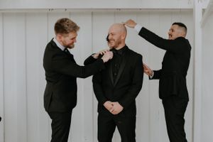 Wedding party members help adjust each other's bowties and formal attire before the ceremony.