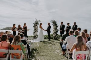 Outdoor wedding ceremony overlooking water with guests seated in white chairs.