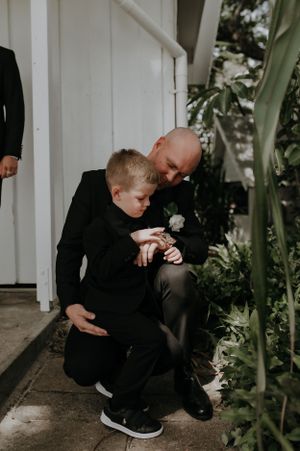 A touching moment between an adult and child in matching black formalwear next to tropical plants.
