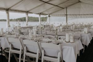 Wedding reception tent with white tables and chairs elegantly set for dinner service.