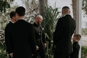 Wedding party members gather outdoors among tropical plants for pre-ceremony preparations.