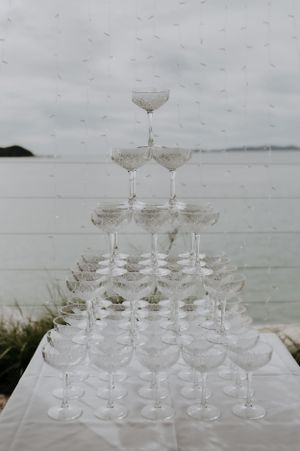 Champagne tower display with crystal glasses arranged in tiers against an overcast waterfront backdrop.