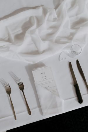 Overhead view of formal place setting with white tablecloth, silverware and menu card.