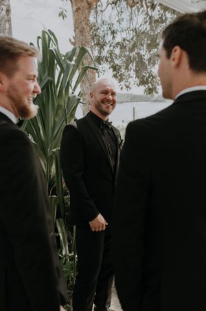 Groomsmen share a lighthearted moment while standing among tropical plants.