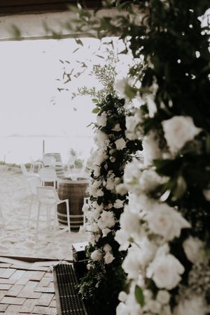 Romantic floral arch with white roses and greenery framing an outdoor wedding venue.