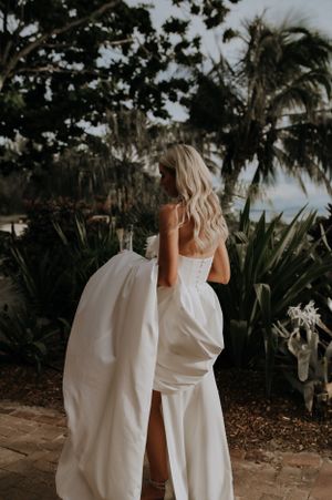 Elegant white wedding dress photographed against tropical palm trees and garden scenery.