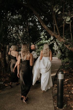 Wedding party walking along garden path beneath trees at dusk.