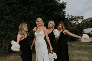Wedding party members share candid moment outdoors with white floral bouquets.